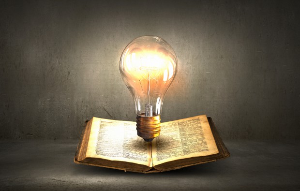 Glass glowing light bulb on opened book
