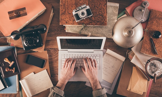 Messy vintage desktop with laptop and male hands typing, top view