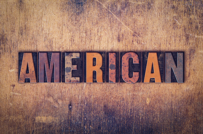 The word "American " written in dirty vintage letterpress type on a aged wooden background.